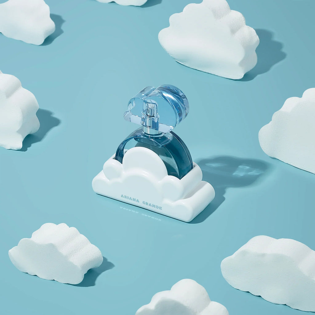Blue perfume bottle on a cloud-shaped stand with white clouds on a light blue background